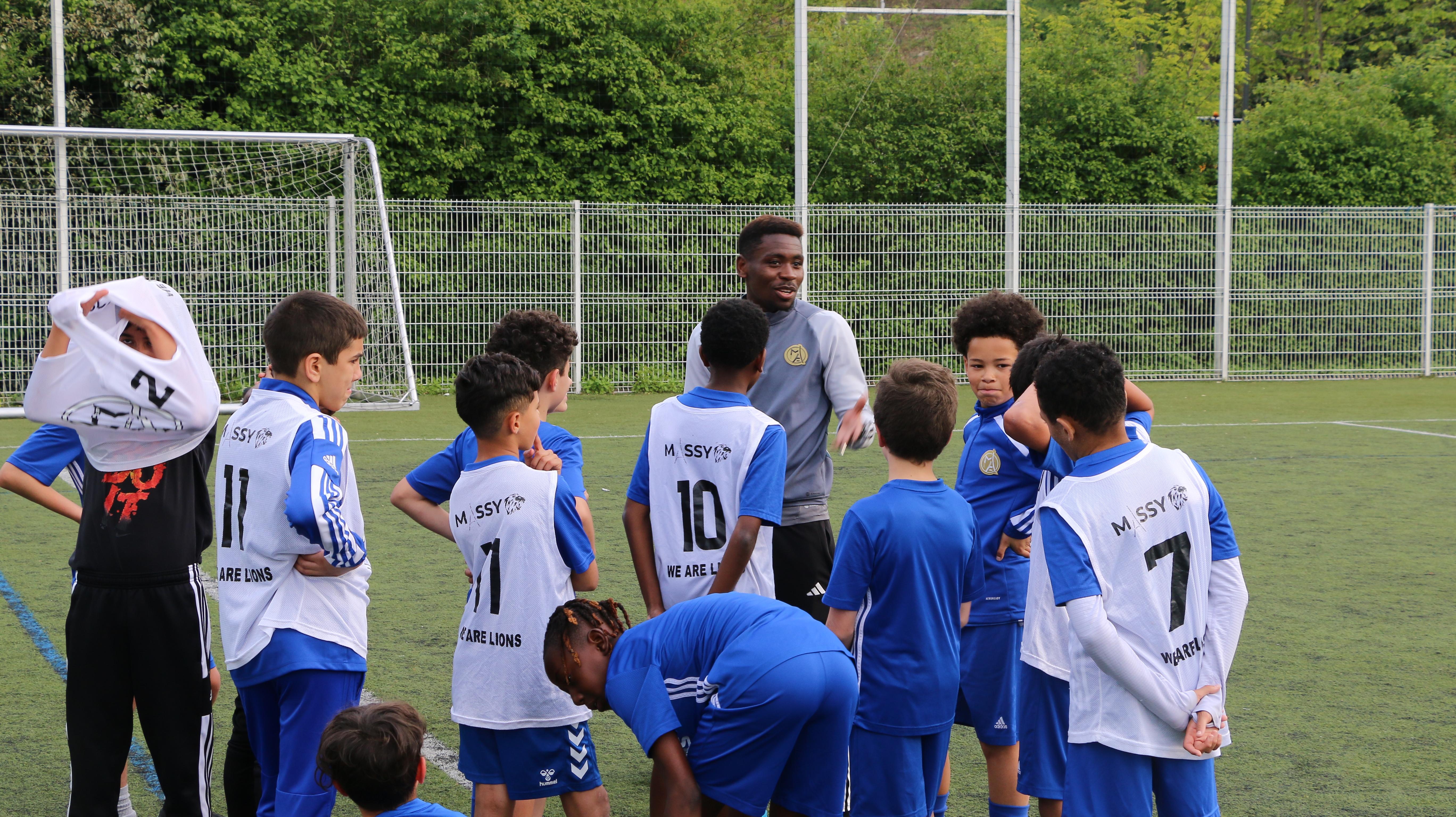 Image d'un coach accroupi avec une feuille et un stylo, entouré de jeunes